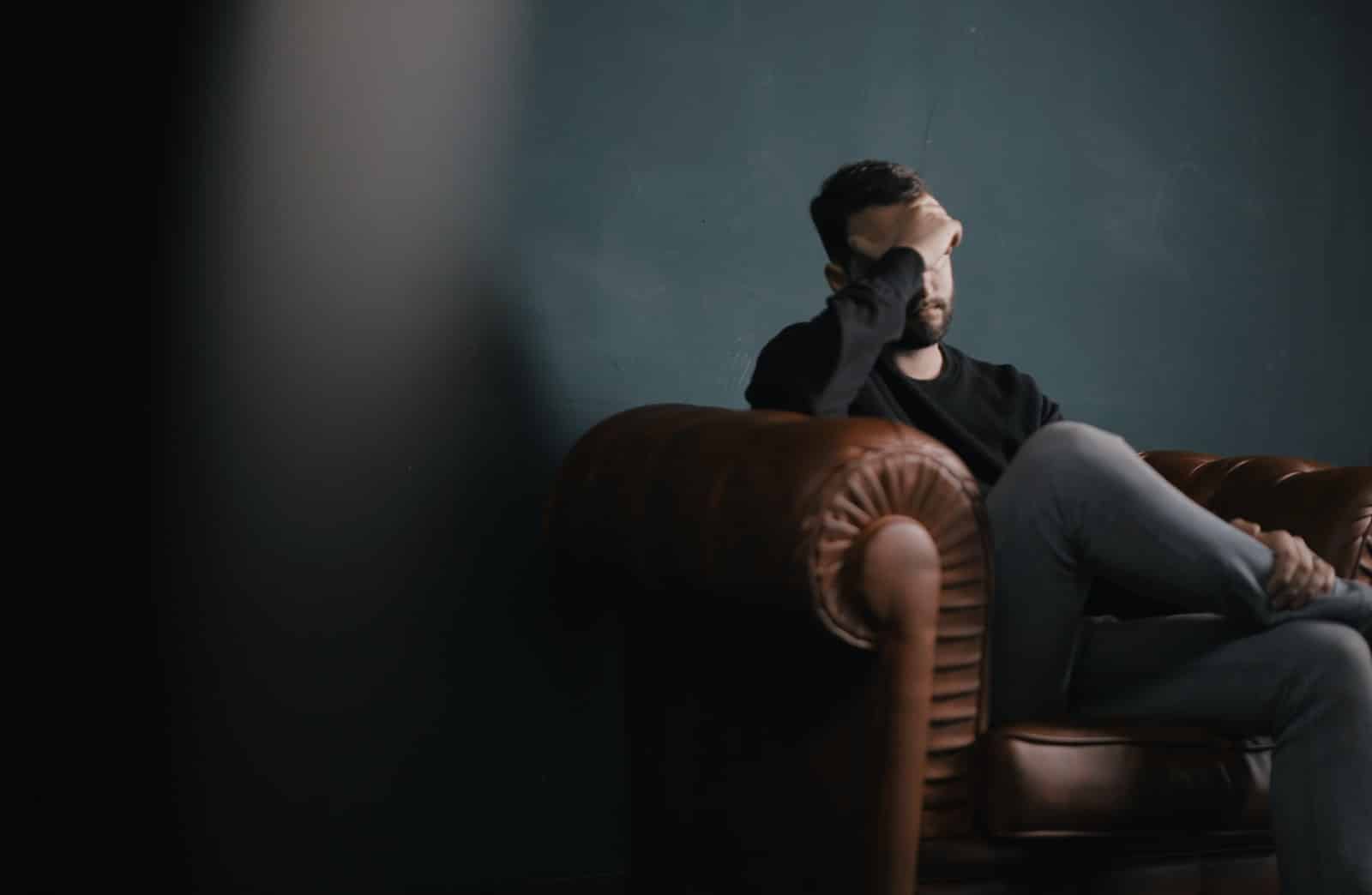 mental health: a man holds his head while sitting on a sofa