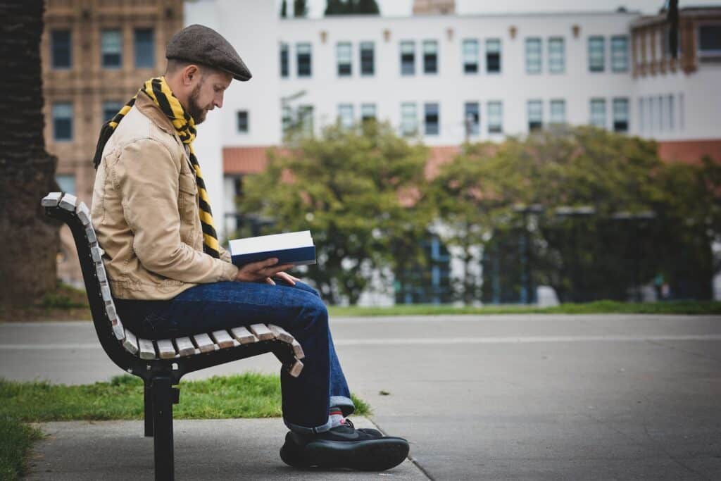 man reading book while sitting on bench outdoors