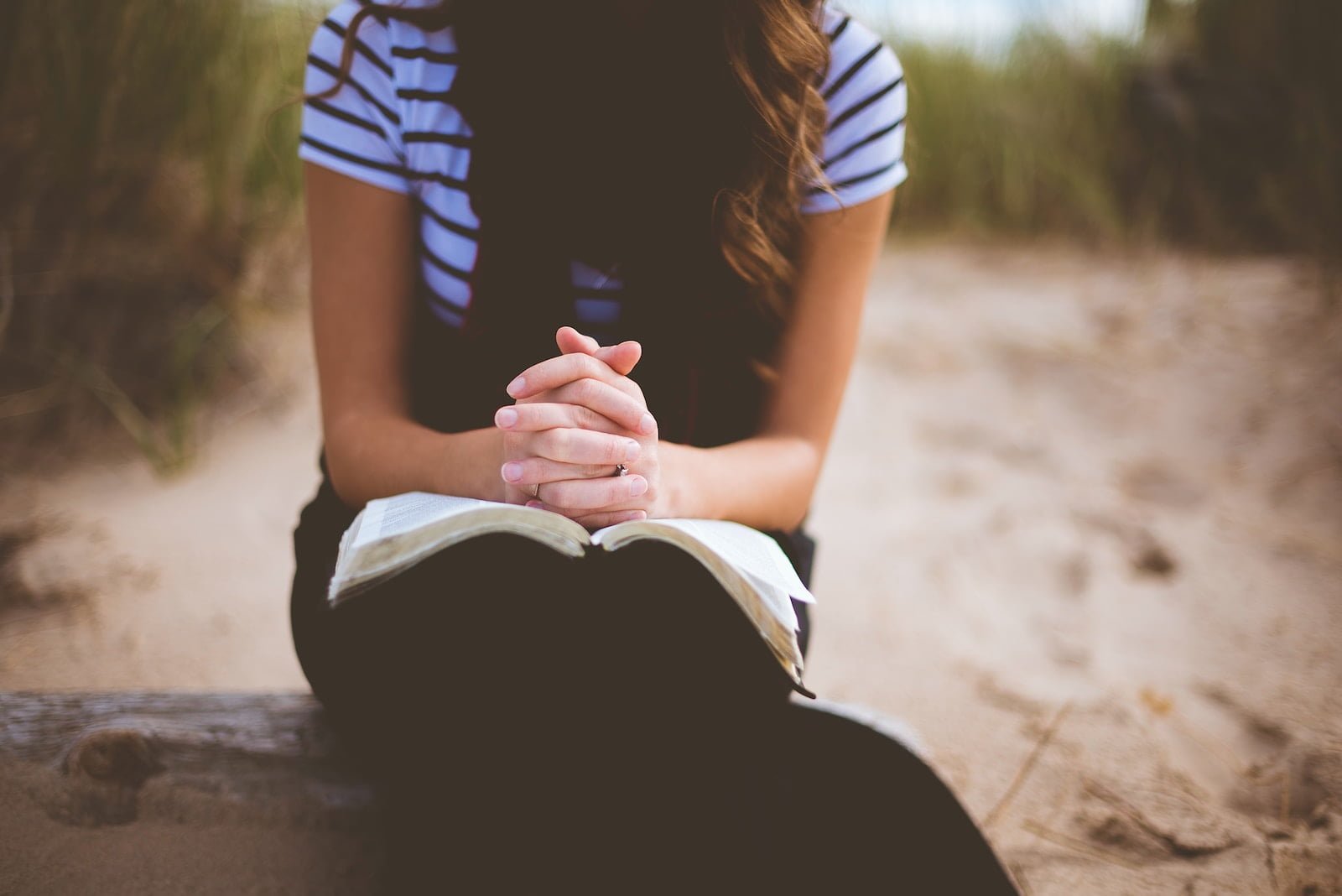 woman sitting on brown bench while studying the bible