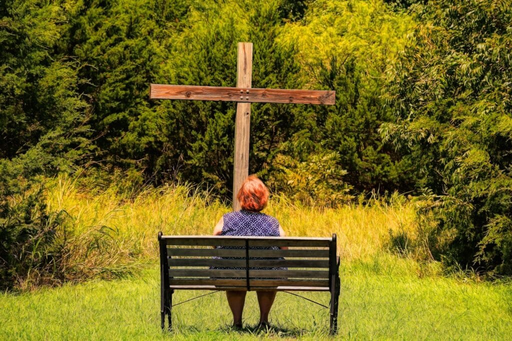 Grace: a woman sitting on a bench in front of a cross