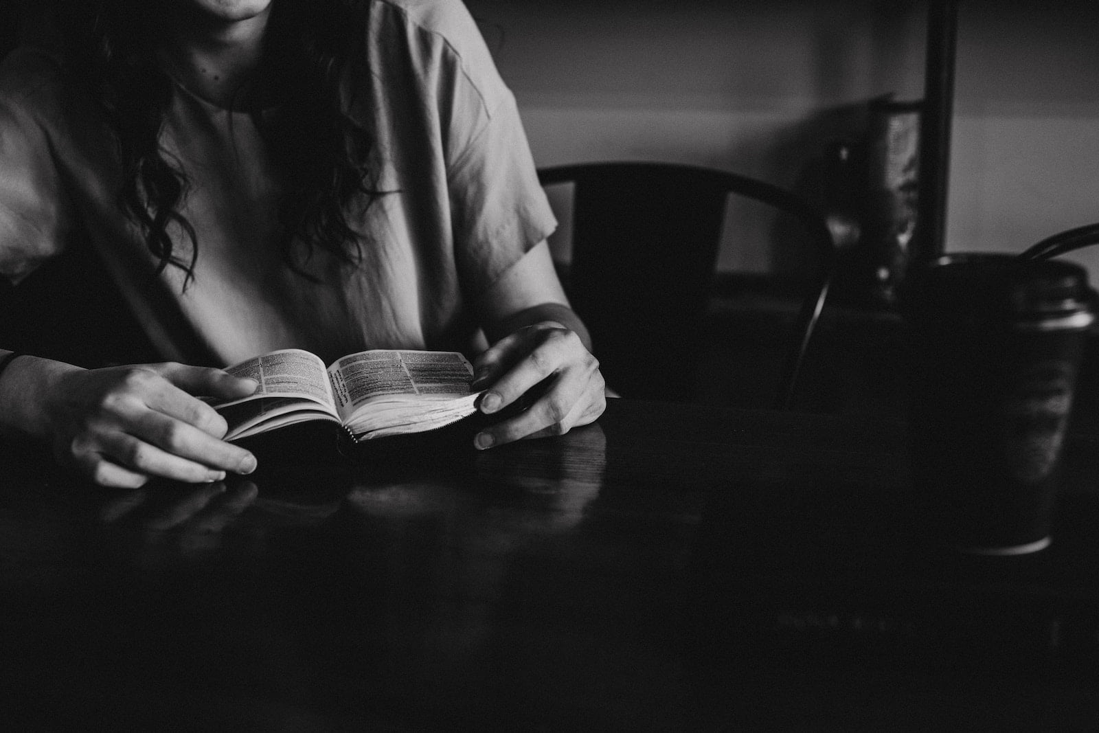 grayscale photo of woman reading a book on wooden table - how to live a godly life